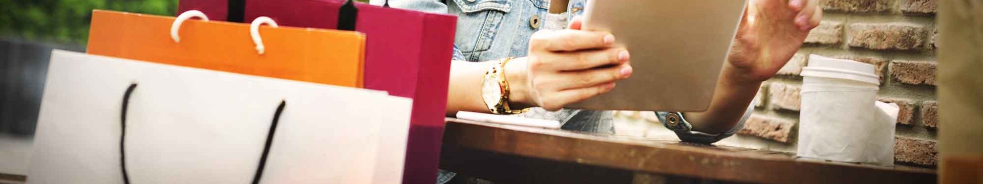 Person sitting with coffee cup, tablet and shopping bags